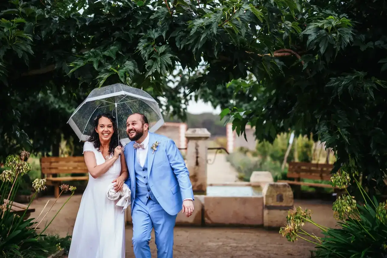 Un couple souriant sous un parapluie transparent, le marié en costume bleu ciel. Une scène qui illustre bien l'expression