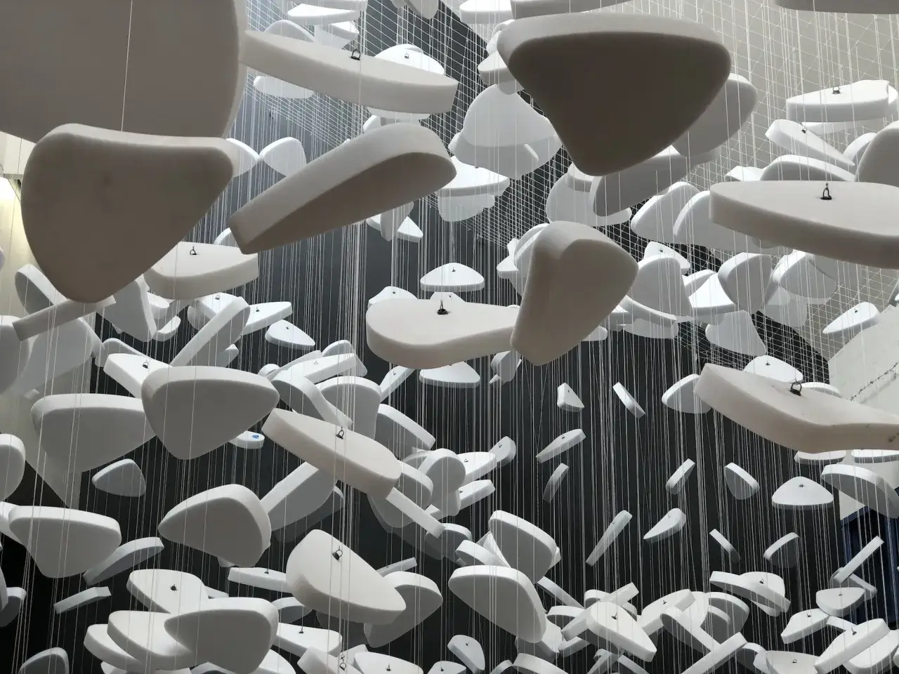 Installation d'art contemporain : des formes blanches flottent dans l'espace, suspendues par des fils fins.