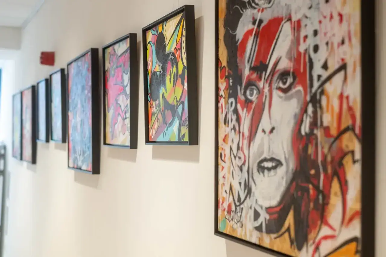 Des toiles colorées, dont un portrait de David Bowie, sont mises en valeur par un encadrement sobre.