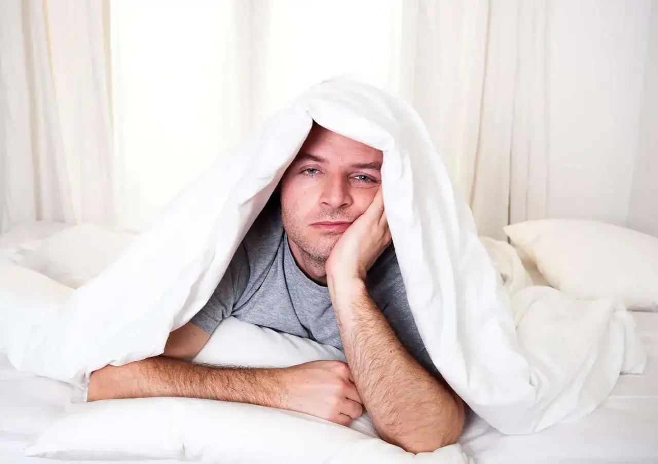 Homme au lit, sous une couette blanche, l'air fatigu&eacute;, il a vraiment du mal &agrave; avoir les yeux en face des trous ce matin.