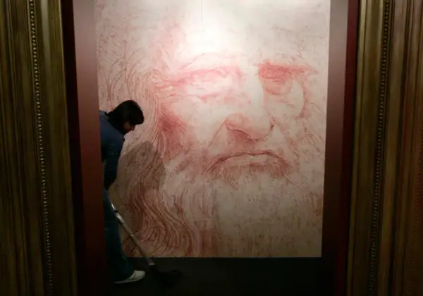 Un homme nettoie le sol devant un portrait de Léonard de Vinci, une œuvre monumentale en sanguine.