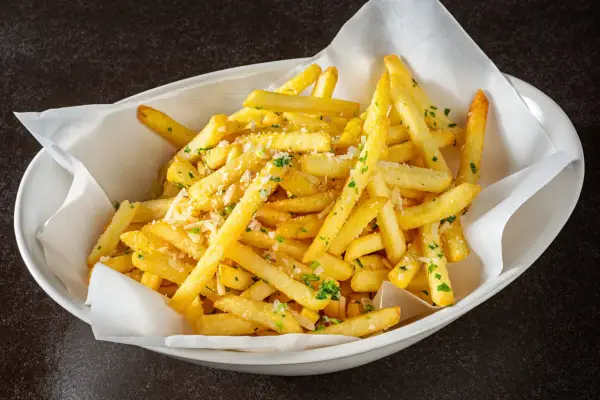 Un plat de frites dorées, parsemées de persil et de parmesan, qui donne envie d'avoir la frite !